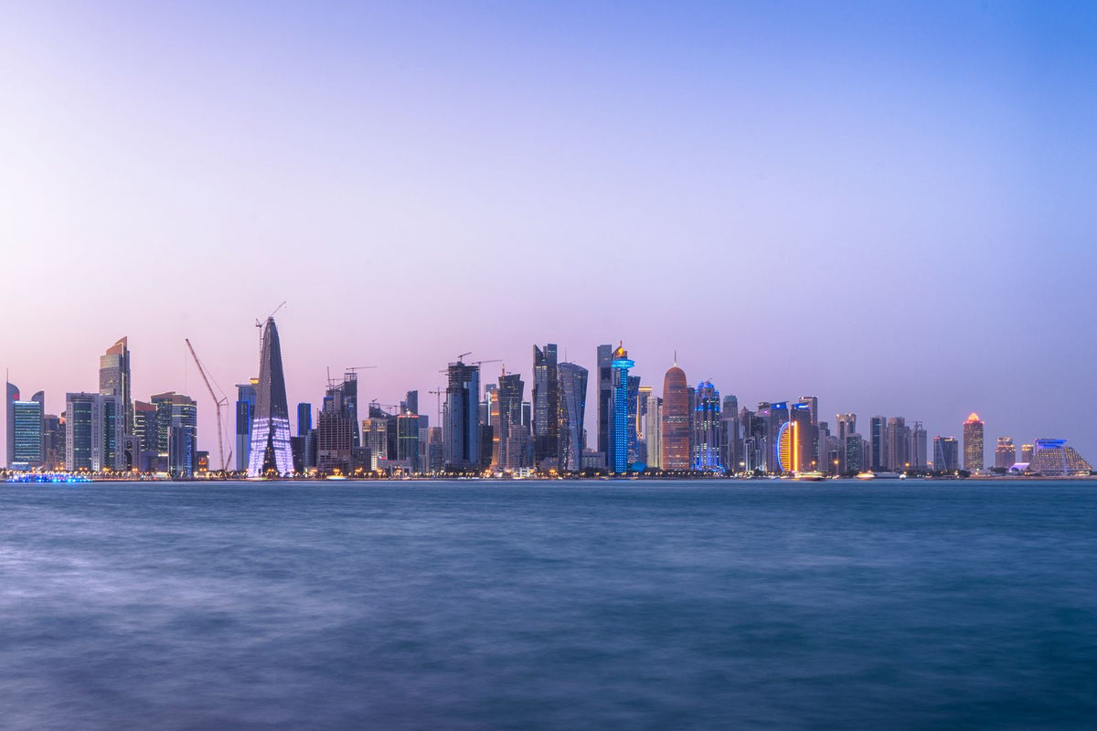 Doha skyline of illuminated towers reflected in the water at blue hour