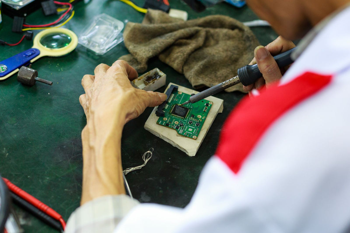 Close-up of a technician using a soldering iron on an electronic circuit board, representing hardware prototyping and R&D