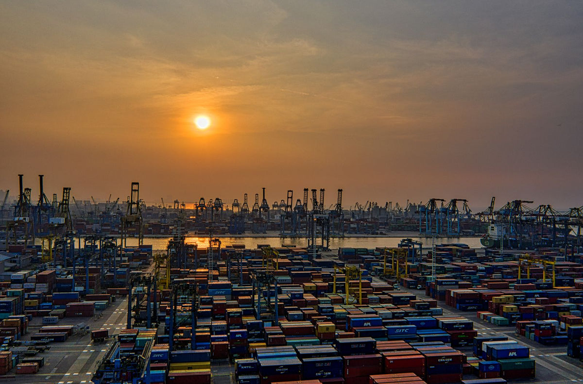 Aerial view of a seaport at golden hour with stacked shipping containers and cranes