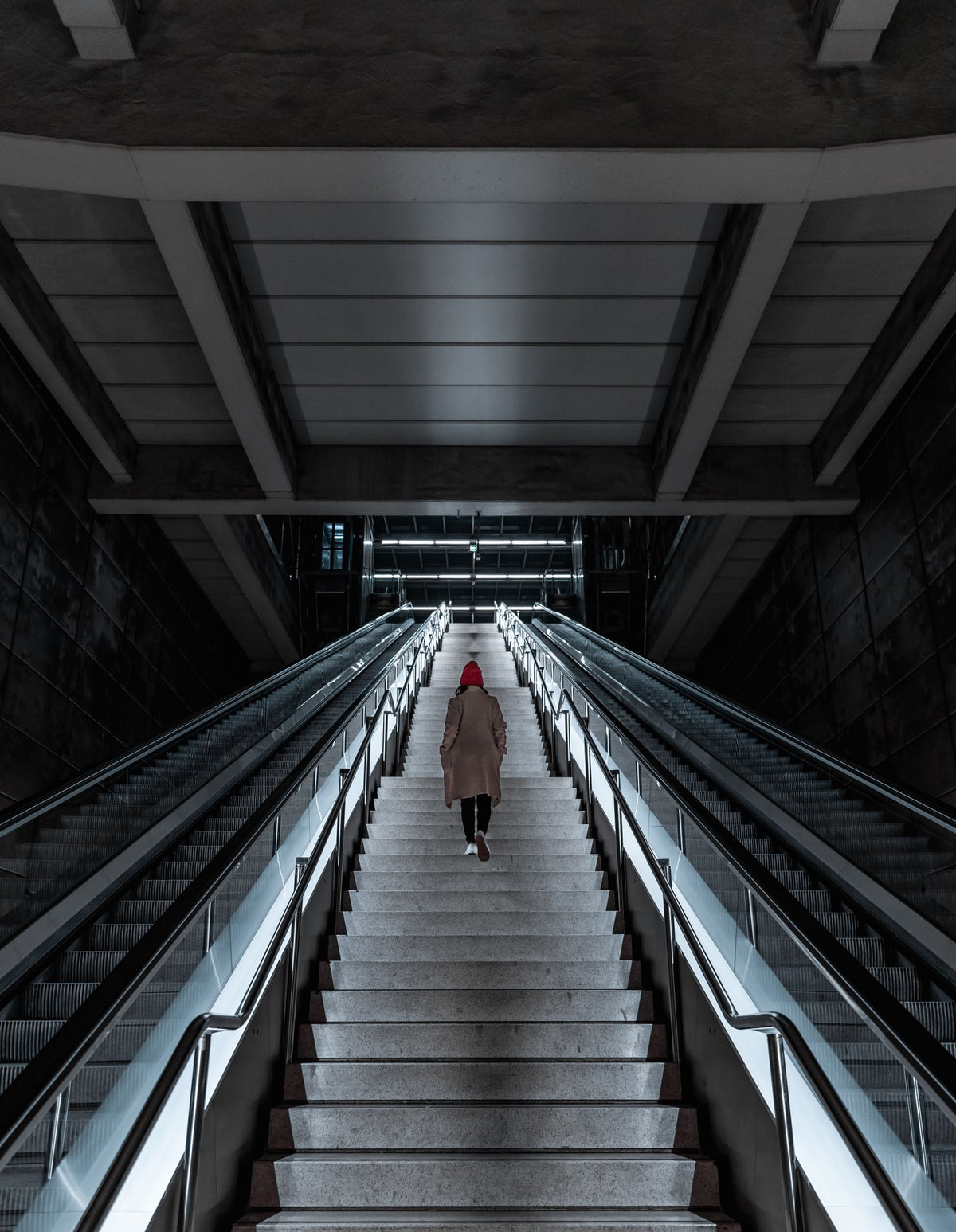 A person climbing a long concrete staircase in a modern underground station, symbolising the step-by-step climb of starting a business