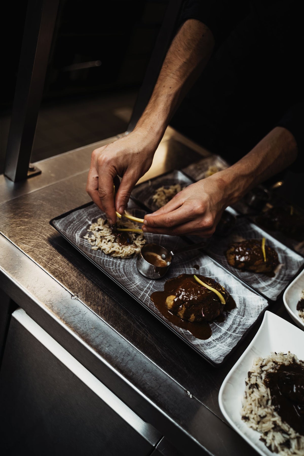 Close-up of a chef's hands arranging plated dishes in a restaurant kitchen