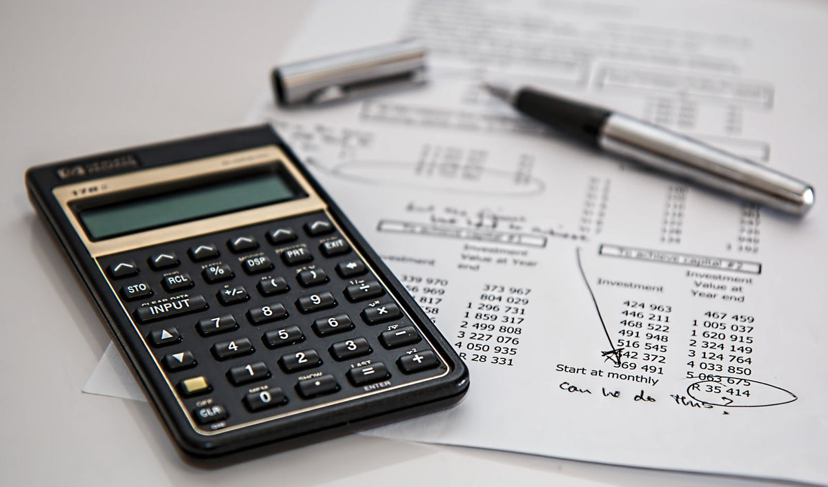 Calculator and pen resting on printed financial documents, representing investment terms and risk calculations