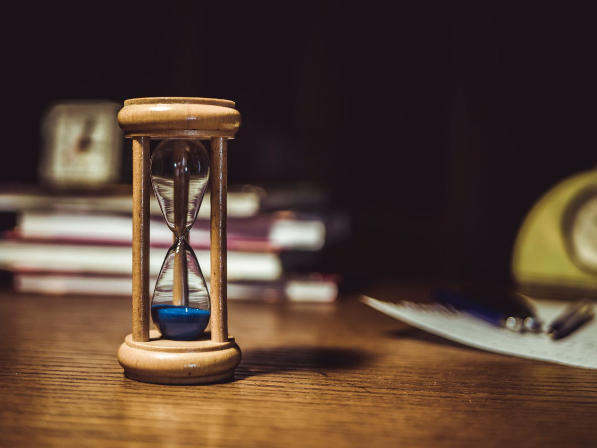 Wooden hourglass with blue sand running on a desk, representing cloud credits with a fixed expiry date