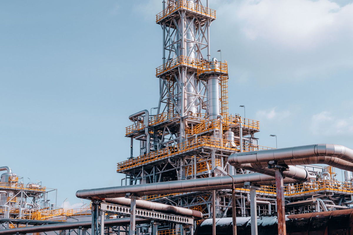 Oil refinery plant with steel towers and intricate pipelines under a blue sky
