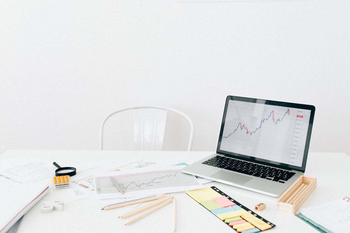 Laptop showing financial charts on a white desk beside documents and sticky notes