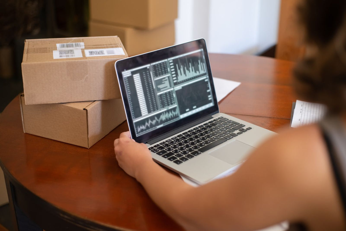 Small business owner reviewing online sales charts on a laptop beside packed cardboard boxes