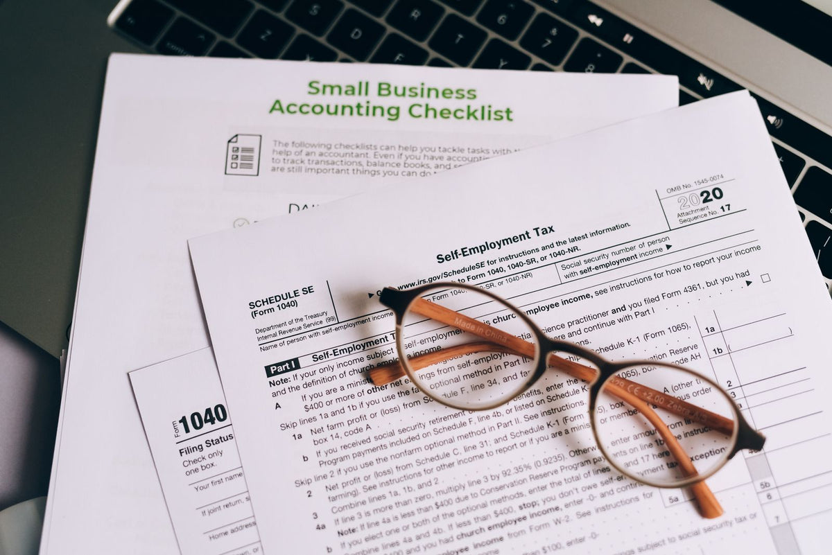 A pair of eyeglasses resting on printed tax and accounting documents next to a laptop